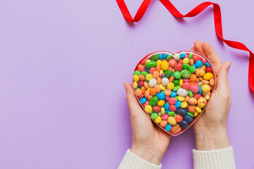 Female hands with delicious candies in box on color background
