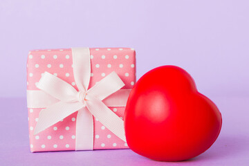 gift box with red bow and red heart on colored background. Perspective view. Flat lay