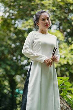 Portrait of Vietnamese woman in white ao dai resting near the lake in the park