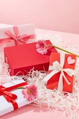 A red podium with empty space placed on a pile of kraft paper with beautiful gift boxes and pink flowers. Concept scene stage showcase for new product, promotion sale, cosmetic presentation