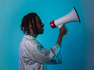 African American man dons traditional attire, passionately utilizing a megaphone against a striking blue background, symbolizing his vocal and cultural empowerment in the pursuit of social justice and