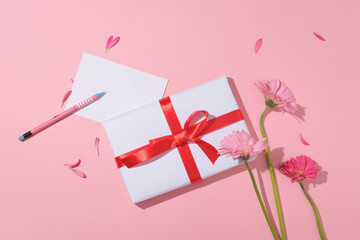 Pretty gift wrapped in white paper with red ribbon. Flowers, a white paper with copy space displayed with a pencil. International recognition of women's rights began with movements in the US