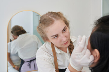 Obraz premium Young Asian woman undergoing eyebrow correction procedure in beauty salon, closeup