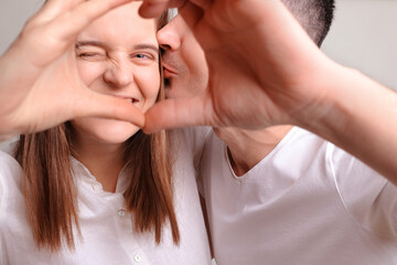 Couple making heart shape with hands and looking through it at camera expressing positive emotions and warm feelings loving couple isolated over gray background