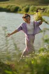 Amidst gentle waters, the mature Asian woman stands with a bouquet, her stance a meditative harmony with the environment.