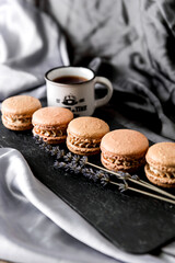 Macaroons arranged on a plate on a gray background with a cup of coffee