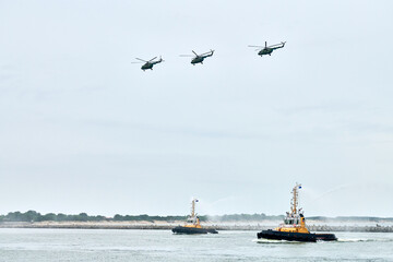 Three Russian military helicopters armed with missiles flying ashore over tugboats, airborne...