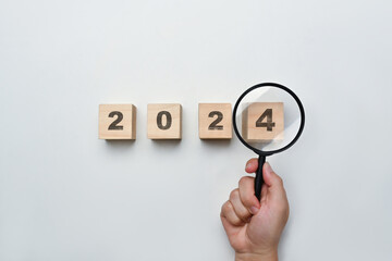 Magnifying glass and wooden cubes with 2024 year number on white background. New year goal and resolution concept