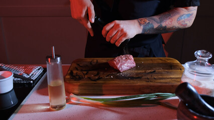 The chef sprinkles a piece of raw meat with pepper. Working environment on the kitchen table