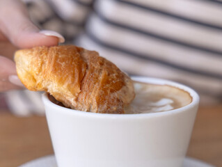 tasty delicious croissants and coffee cappuccino cup with hearts from milk foam in cafe, french pastry.woman hand girl dipping croissant in cup.good morning concept, cozy warm photo