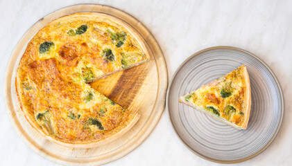 tasty broccoli and salmon pie or traditional french quiche on wooden round board.slice served on plate, section view. delicious ingredients baked on dough sheet.close up,top views