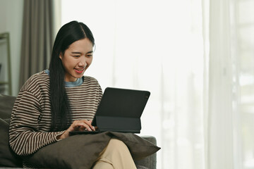 Beautiful Asian woman chatting on digital tablet browsing internet or working online at home