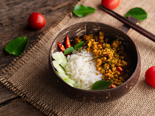 Rice topped with stir fried pork with yellow curry paste in bowl on wooden table background. Traditional Thai southern food