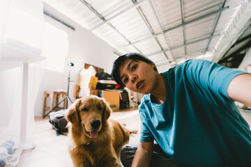 A real Asian man takes a selfie with a 7-month-old golden retriever looking happily at the camera at home. - Powered by Adobe