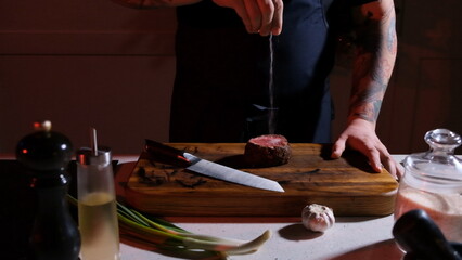 The chef's hands prepare a dry aged beef steak with a large piece of fillet, adding salt and pepper...