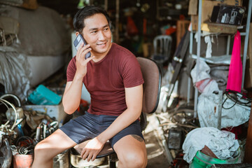 Fototapeta na wymiar Handsome young mechanic making a cell phone call sitting on a chair in an old garage