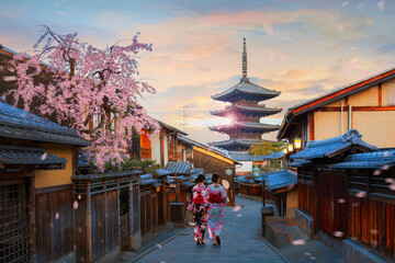 Fototapeta premium Scenic cityscape of Yasaka pagoda sunset in Kyoto with a young Japanese woman in a traditional Kimono dress during full bloom cherry blossom and scatter sakura petals