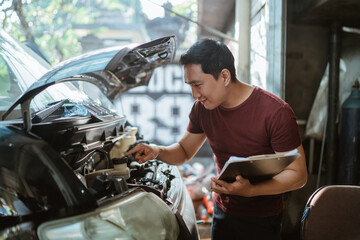 young male mechanic checks brake fluid while holding a clipboard at a repair shop