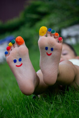 Fototapeta premium Children's legs with a pattern made of paints are smiling on the green grass