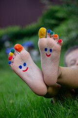 Fototapeta premium Children's legs with a pattern made of paints are smiling on the green grass