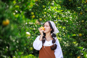 asian woman in vintage dress sniff orange fruit in her hand in the orchard during the harvest.