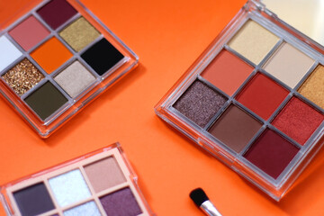 Colorful eyeshadow palettes and make up brush on orange background. Selective focus.