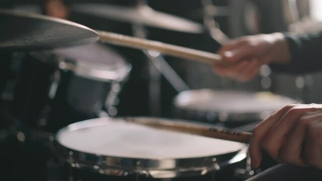 Drummer plays drums in music studio at band rehearsal, close up with selective focus.