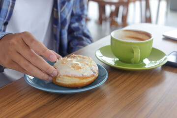 Close up of male hand eating sweet donut in cafe