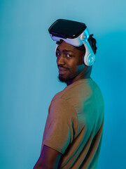 In a futuristic visual, an African American man stands isolated against a striking blue backdrop, adorned with VR glasses that transport him into a cutting-edge virtual reality experience, merging