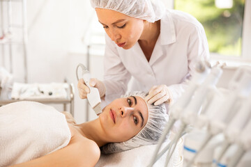 Young woman cosmetologist performs hardware facial exfoliating procedure to young female patient