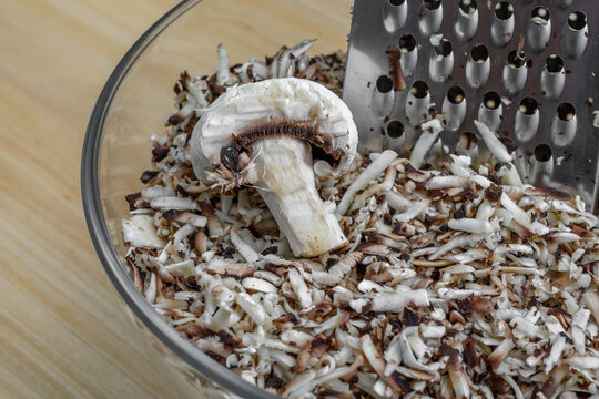 Grzyby białe pieczarki ścierane na stalowej tarce kuchennej do szklanej miski