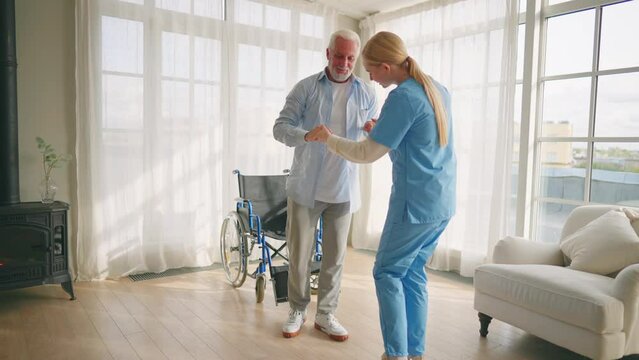 Nurse helps old wheelchair man to walk. Physical therapist woman provides medical help support to senior male training studying to go. Recuperation after trauma, temporary paralysis, support concept.