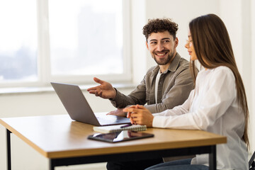 Fototapeta premium Two young businessmen and businesswomen sitting in the office, talking and surfing the internet together with a laptop
