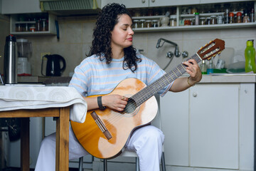 young latin woman practicing acoustic guitar at home