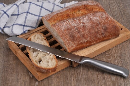 Pain pav&eacute; rustique avec une tranche coup&eacute;e sur une planche &agrave; pain avec un couteau &agrave; pain en gros plan.
