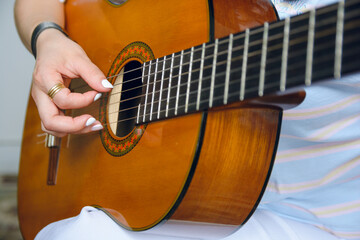 unrecognizable young woman playing acoustic guitar, focus on hand on strings at soundhole of guitar