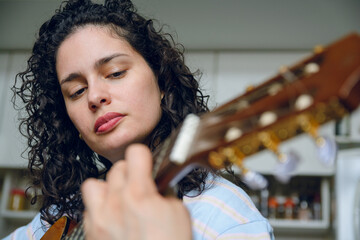 closeup of young latin woman playing guitar concentrating watching how she makes chord