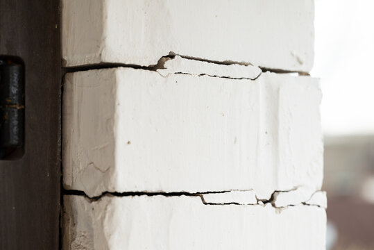 Brick wall of a house with cracks. House with many cracks between bricks near door, building foundation problems