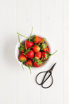 Strawberries, in a bowl, on a white wooden table. Top view.