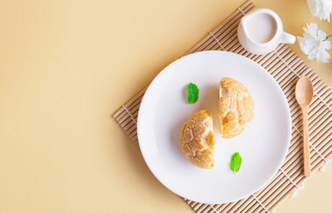 Top view of half cut soft choux cream puff custard flavor in white plate on beige background. Baked Goods style and Minimalist product concept