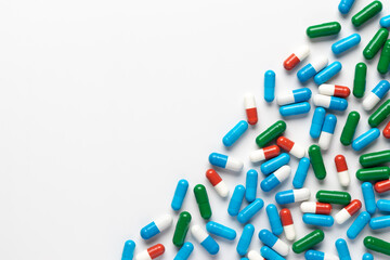 Spilled pills on white background, top view, copy space. Heap of dietary supplements, various colorful vitamins, assorted pharmaceutical medical capsules close-up, beautiful pattern. Minimalist design