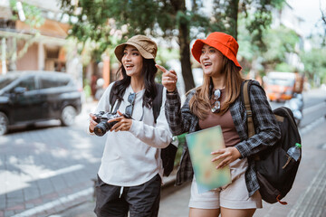 two backpacker girls with pointing fingers looking for tourist destinations carrying cameras and...