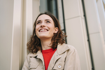 Young Woman in Her 20s Laughing Upwards While Leaning Against a City Building