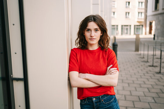 Confident 25-Year-Old Woman Poses with Crossed Arms, Gazing Sternly in Urban Setting