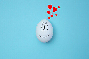 One happy egg on blue background with red hearts above it. Copy space. Emoticons concept. Art...