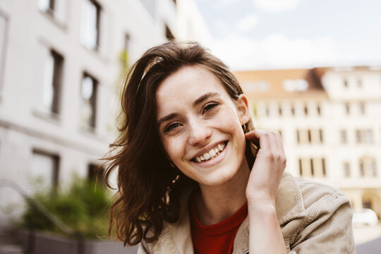 Joyful Young Woman Relaxed in the City, Sitting in Front of a Building, Smiling at the Camera