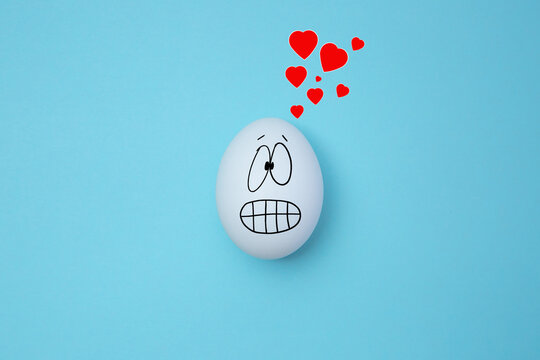 White egg with surprised face with red hearts above it. Isolated on blue background. Copy space. Emoticons concept. Art collage