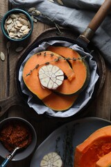 Fresh pumpkin slices with aromatic thyme and garlic in frying pan on wooden table, flat lay