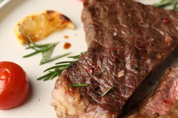 Delicious grilled beef steak, tomato, rosemary and lemon slice on plate, closeup