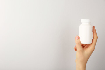 Woman holding blank white jar of vitamins on light grey background, closeup. Space for text